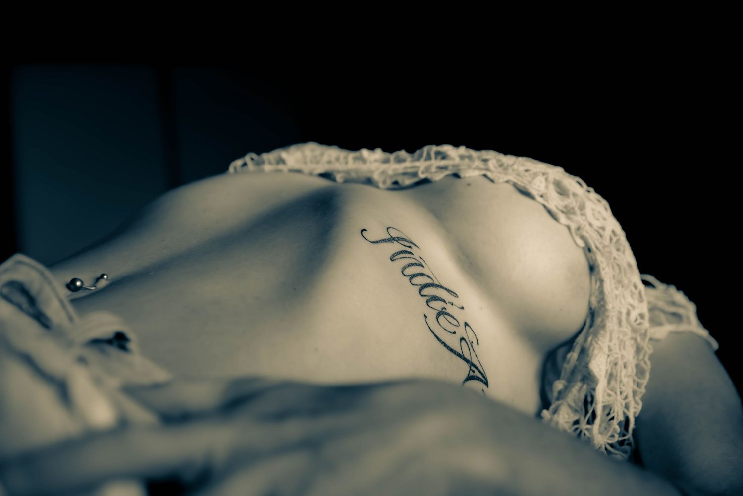 Artistic black and white photo of torso with script tattoo and lace details.
