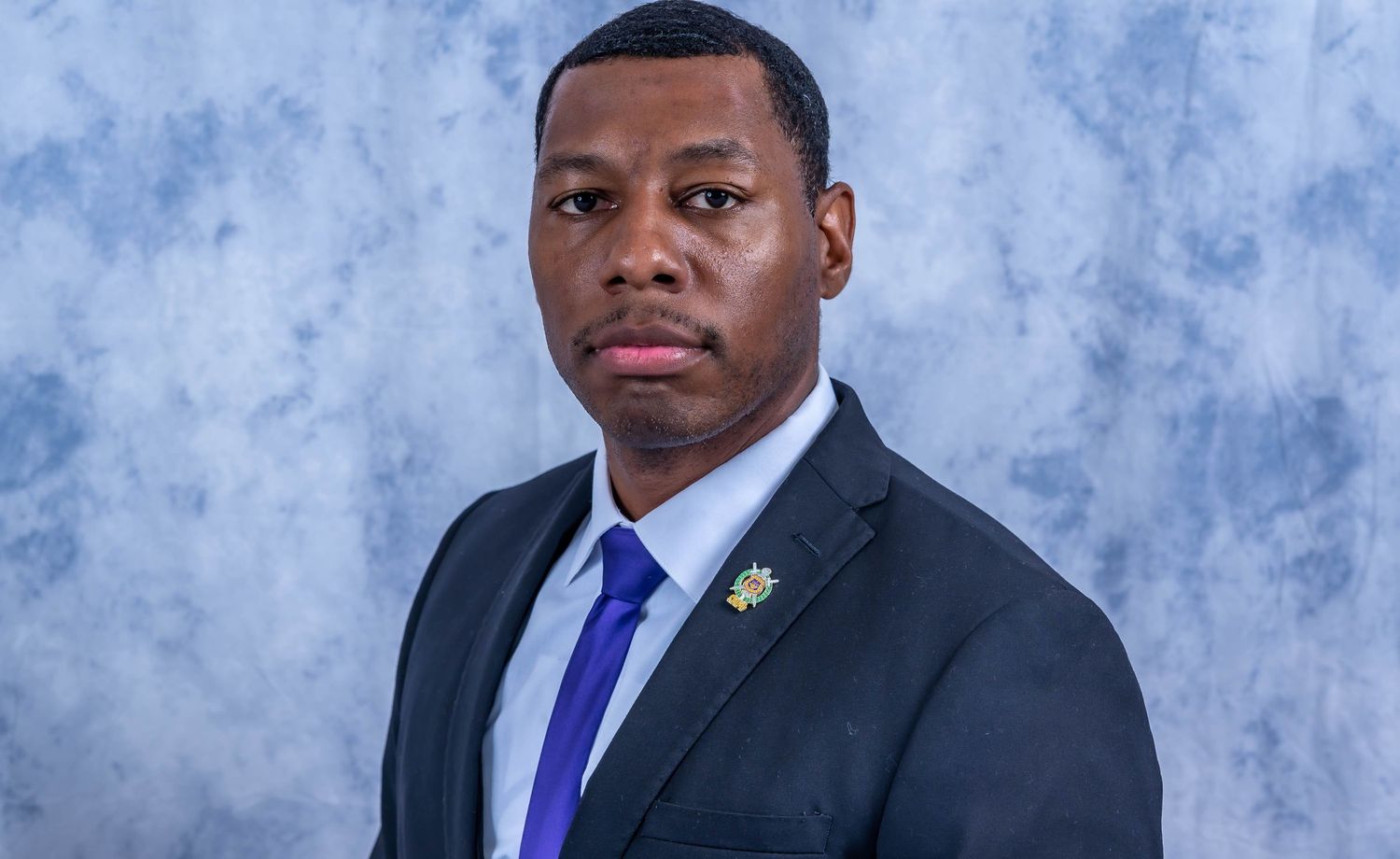 Business professional in dark suit and purple tie poses for formal headshot.