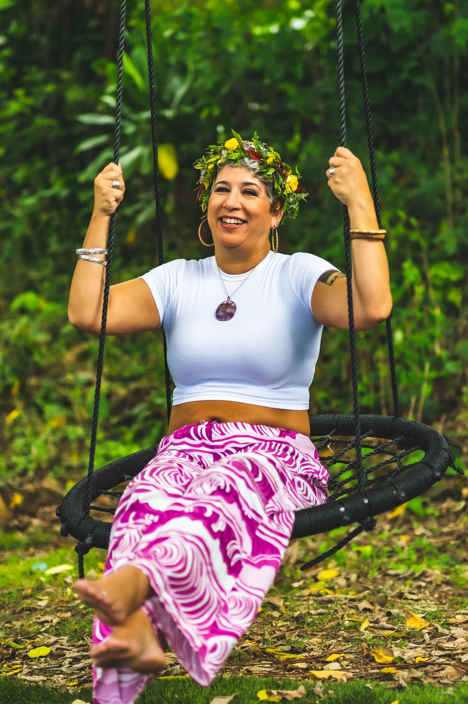 Person wearing white top and pink floral skirt enjoying a swing in a lush garden setting.
