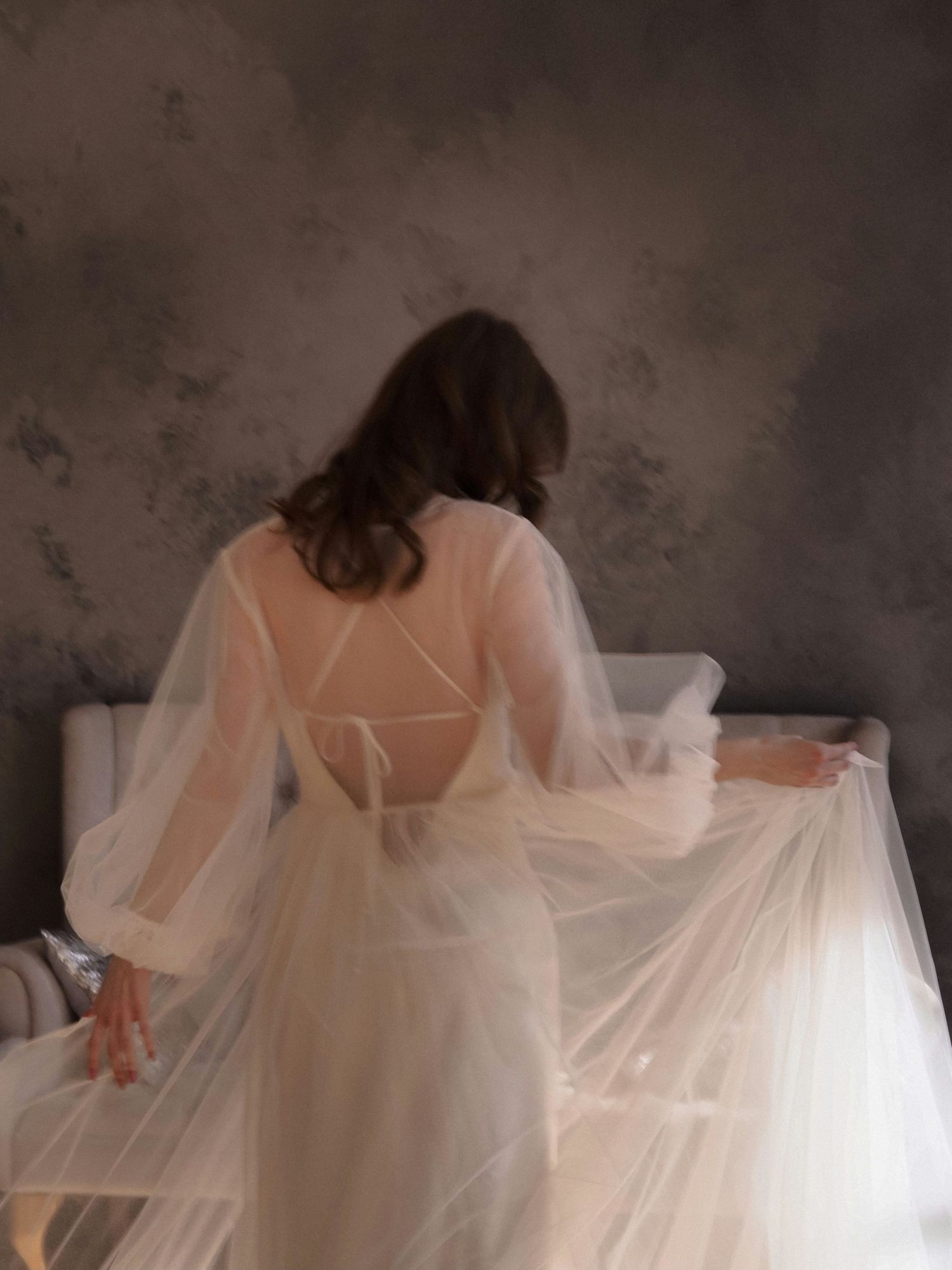 Ethereal white tulle dress photographed from behind in a dark room.