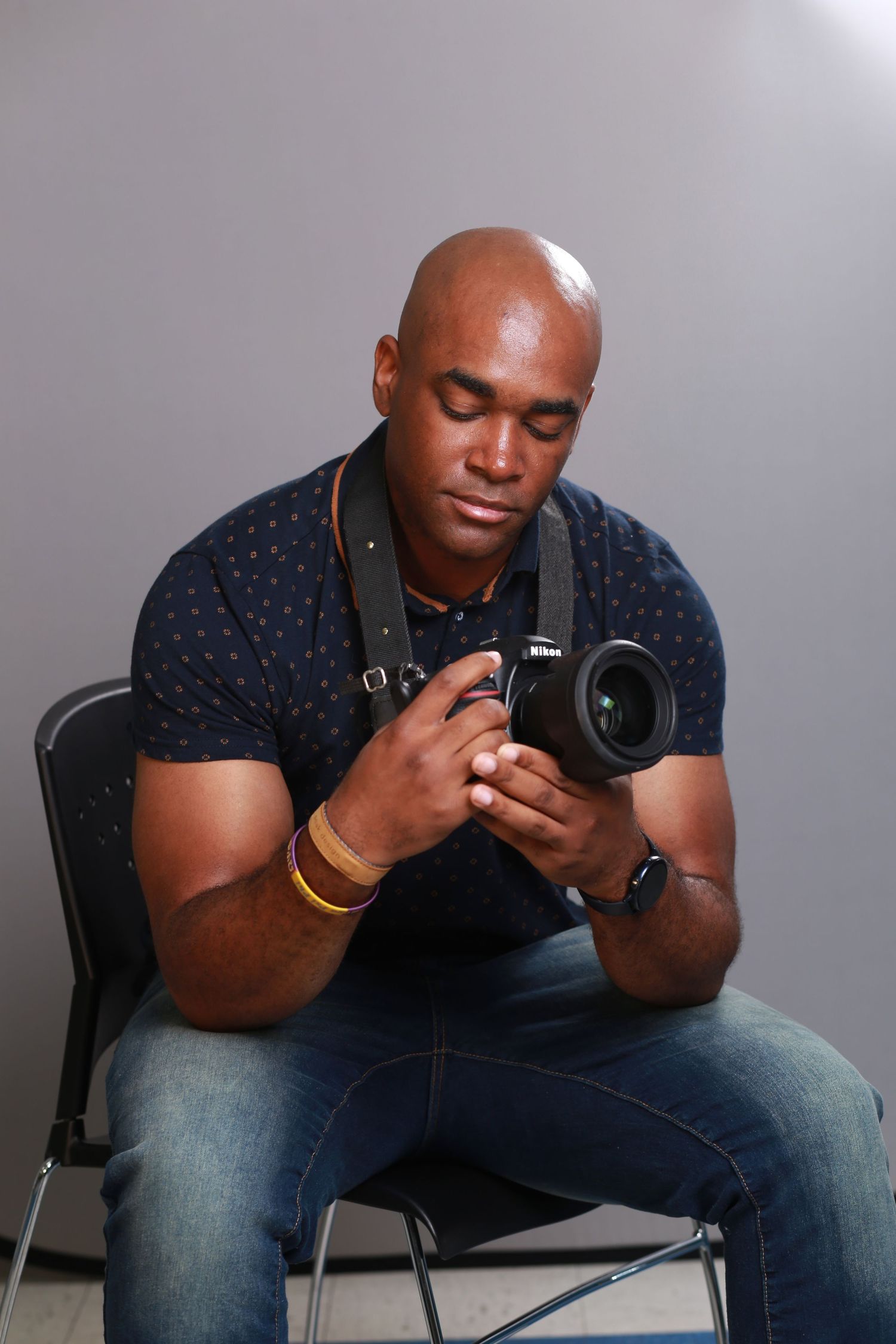 Professional photographer in navy polka dot shirt examines DSLR camera while seated in studio setting.