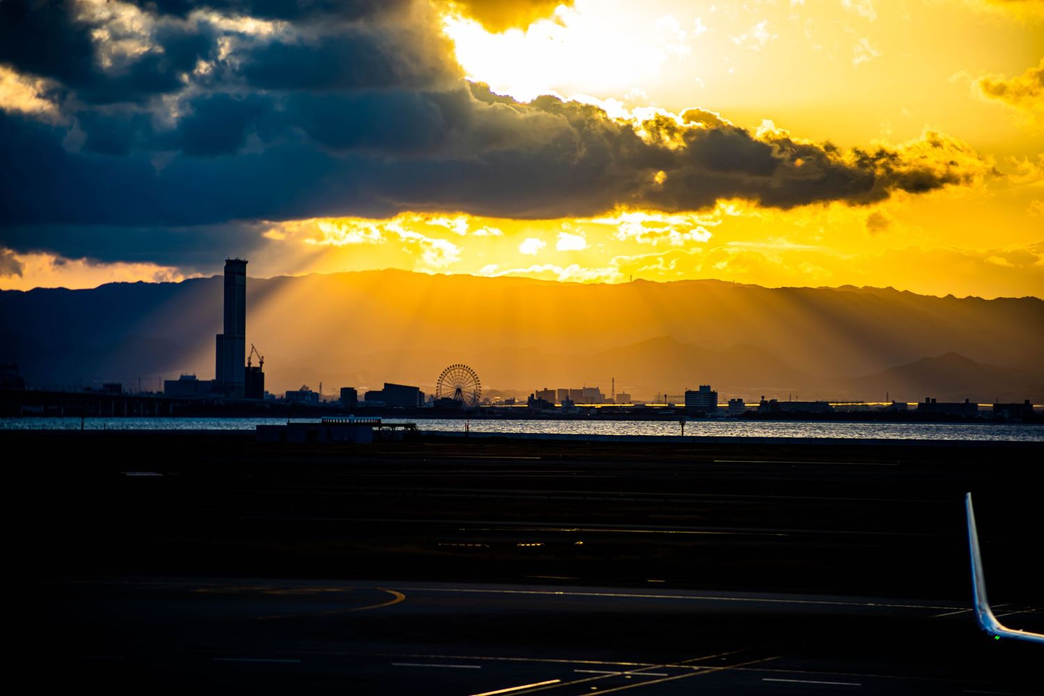 Dramatic sunset silhouettes city skyline with ferris wheel visible in distance.