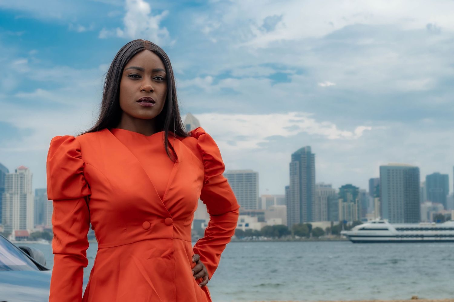 Woman in bright orange dress against city skyline backdrop.