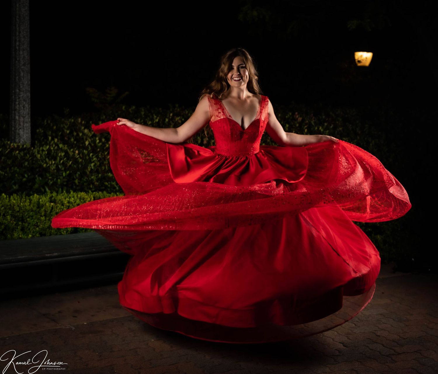 Dancer in vibrant red dress twirls gracefully under outdoor lighting.