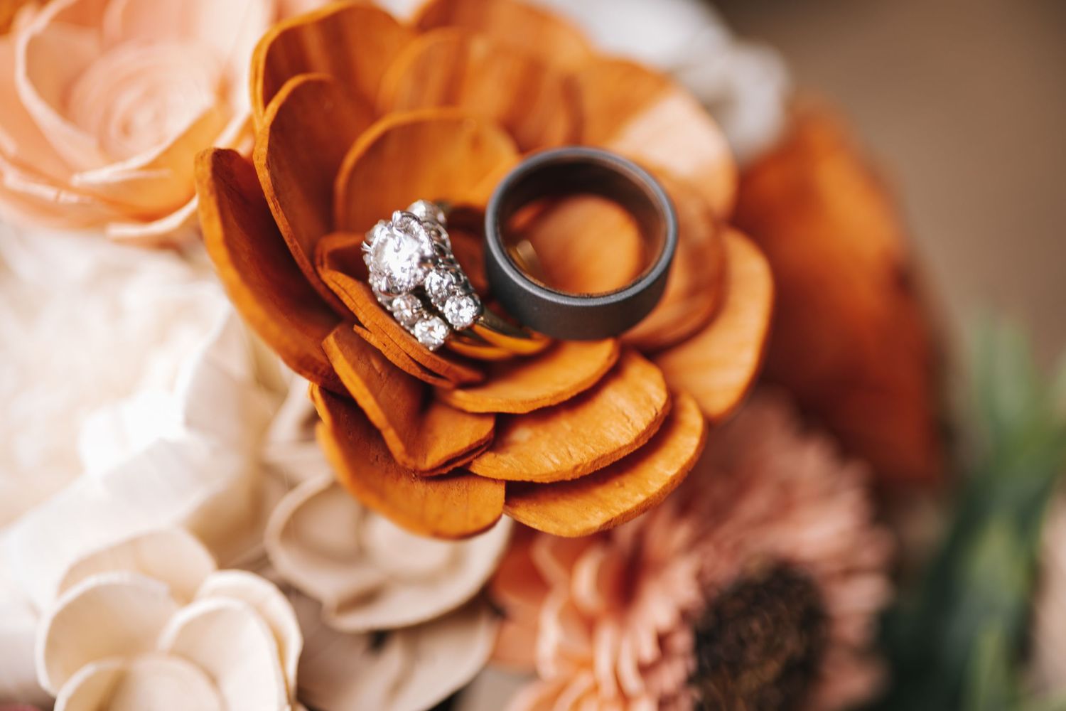 Wedding rings nestled in orange and cream colored roses creating an elegant composition.