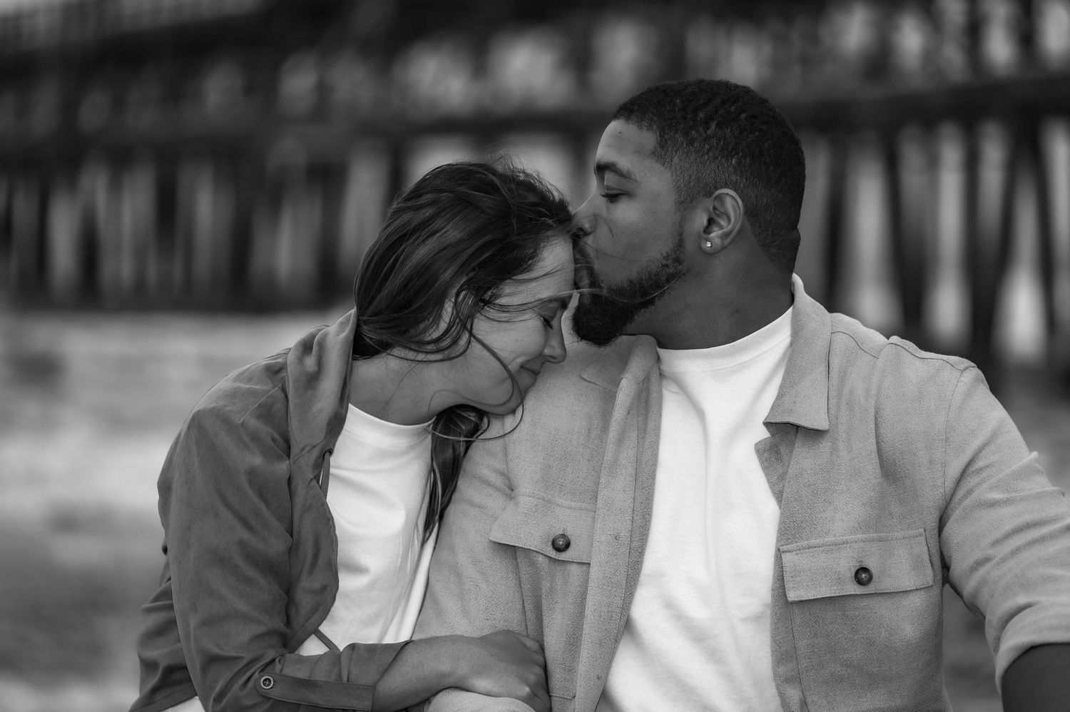 Intimate black and white portrait of couple near beach pier.