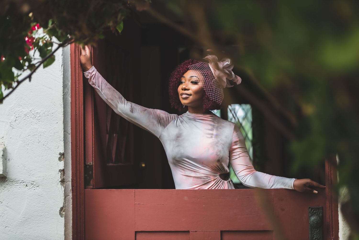 A performer in white attire strikes an expressive pose against a red door frame.