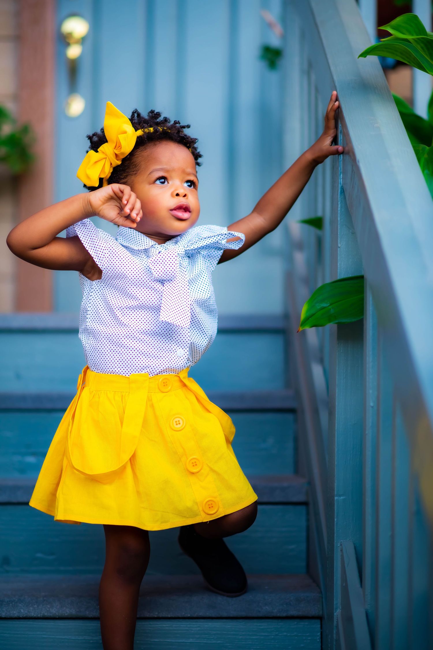 Child in yellow skirt and white top strikes playful pose on blue staircase.