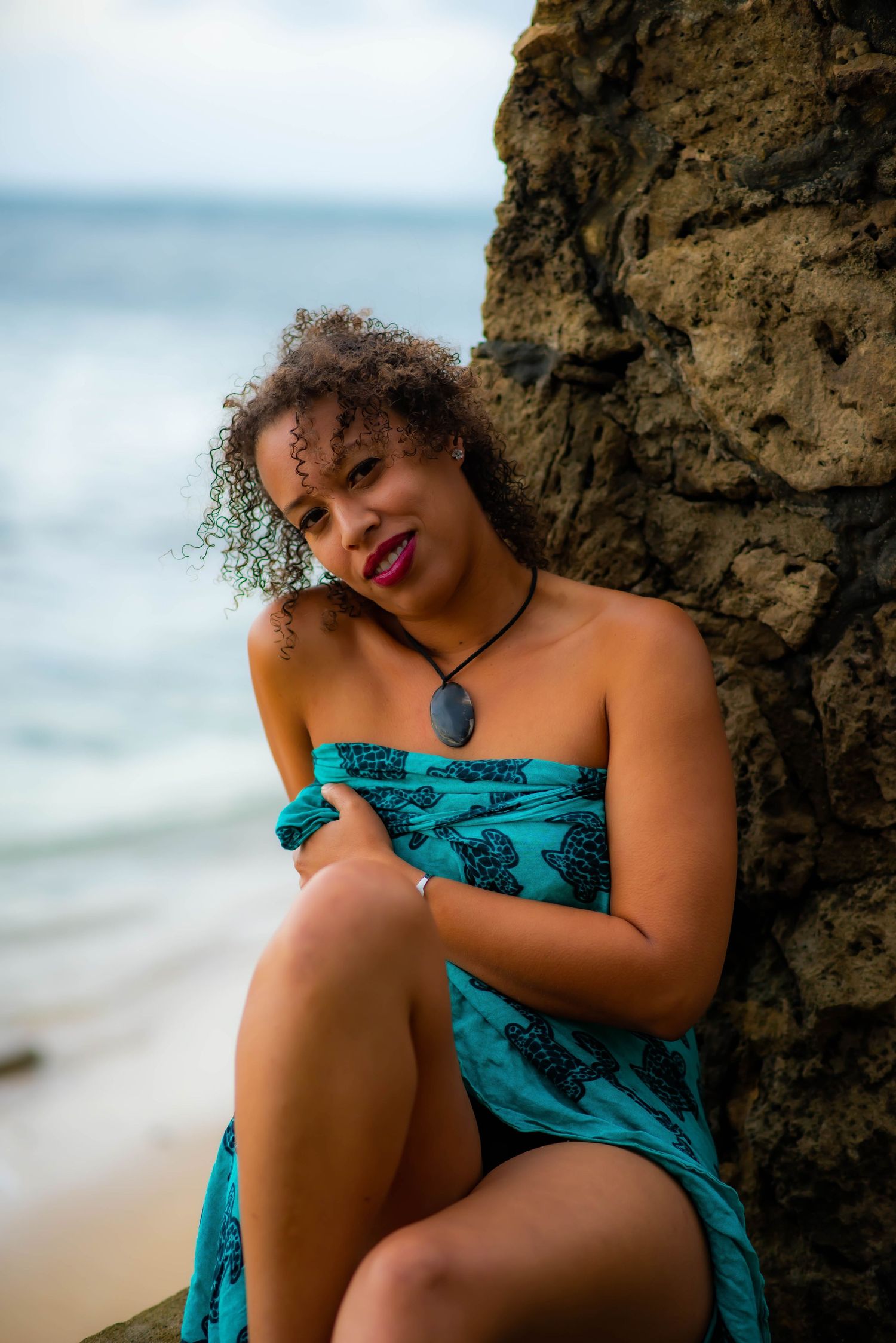 Beachside portrait featuring teal wrap dress against natural ocean scenery.