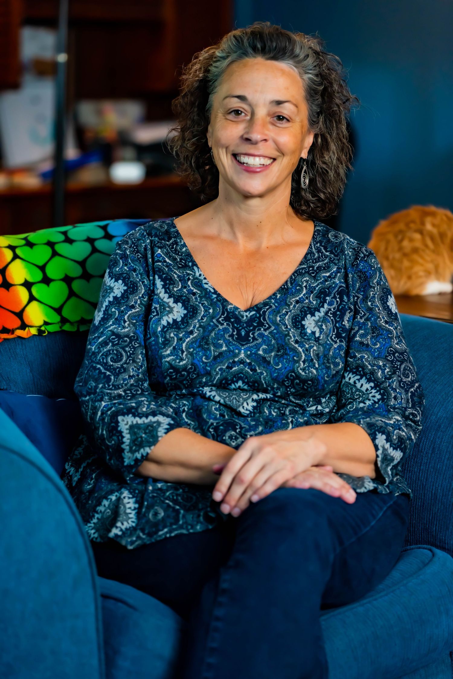Person in blue patterned top relaxing on navy blue couch in dimly lit room.