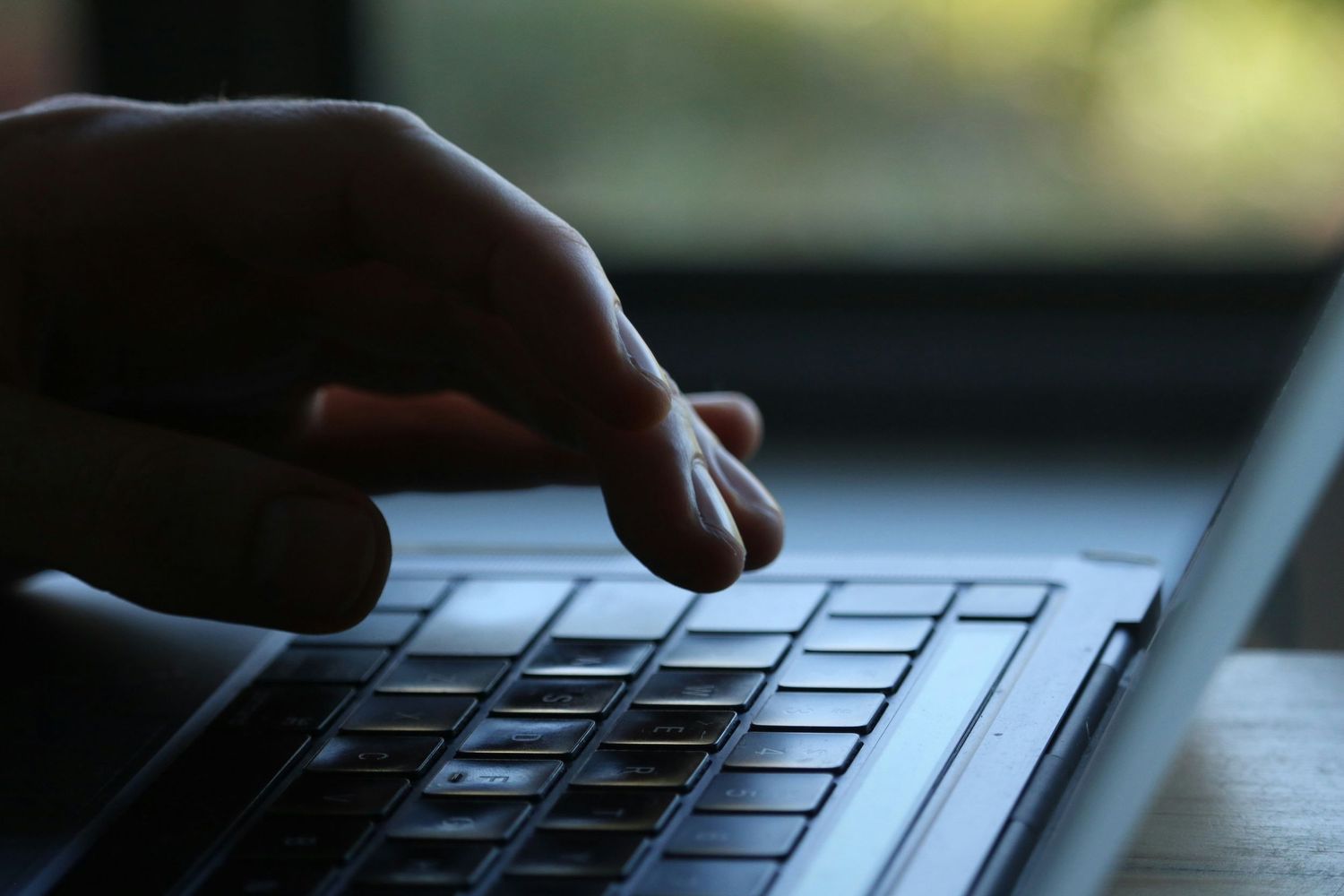 Fingers typing on illuminated laptop keyboard in low light.