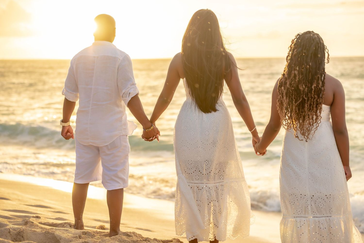 Couple in white clothing walking hand in hand along beach at golden sunset.