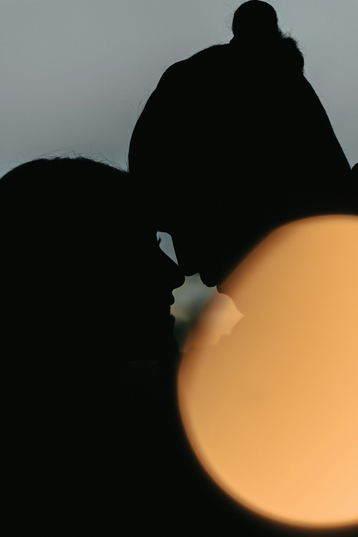 Silhouettes of two people against an orange glowing background creating a romantic mood.