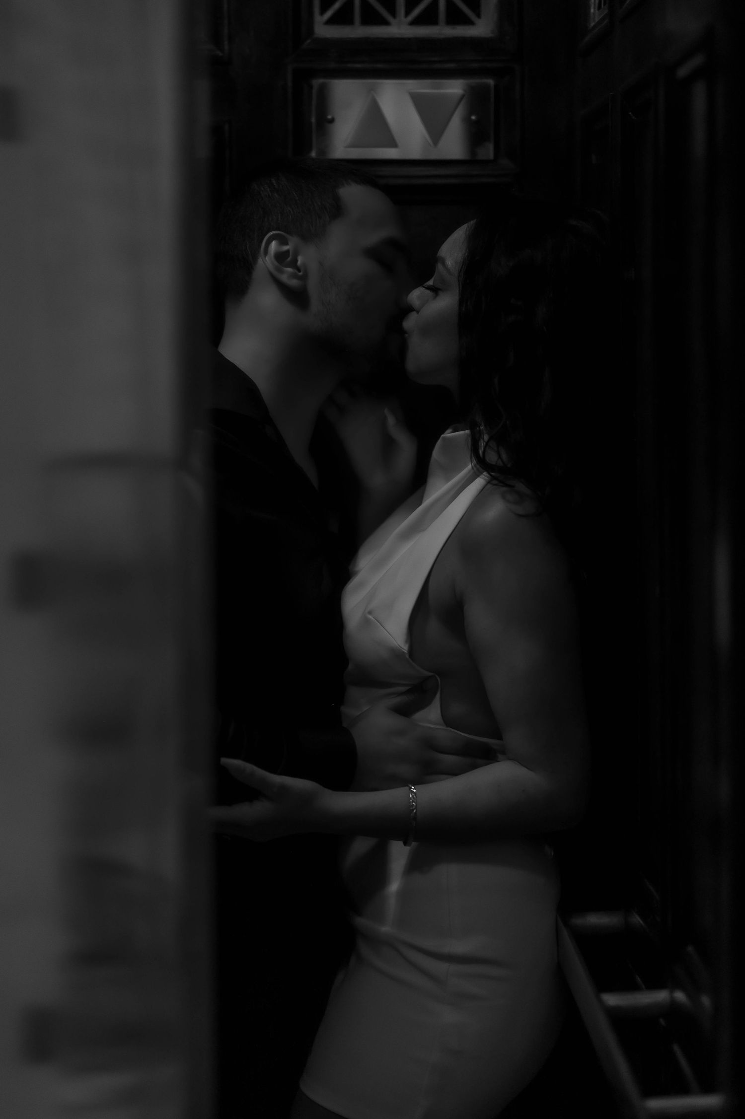 A romantic black and white photograph of a couple in an intimate embrace against a dark background.