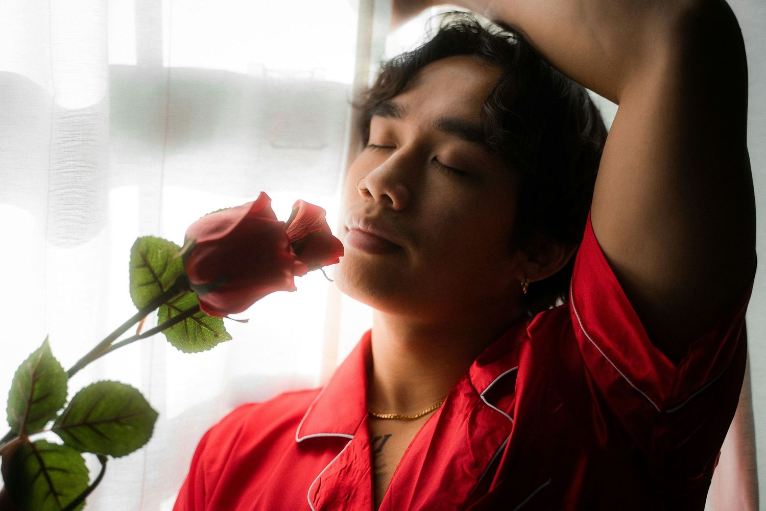 Figure in red posing artistically near a window with green plant elements.