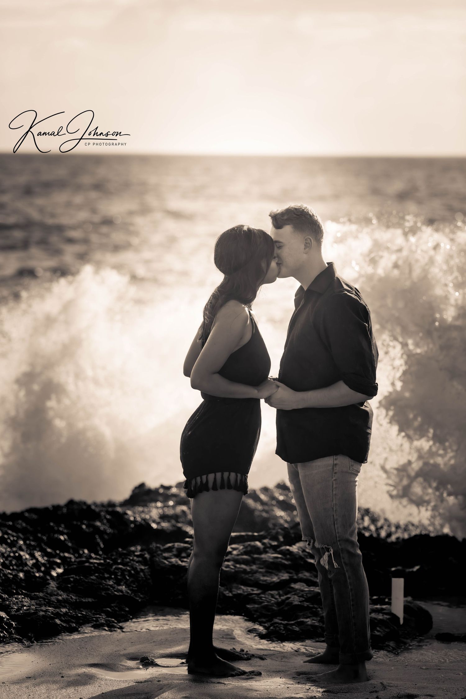 Silhouetted couple shares romantic moment by ocean waves at sunset.