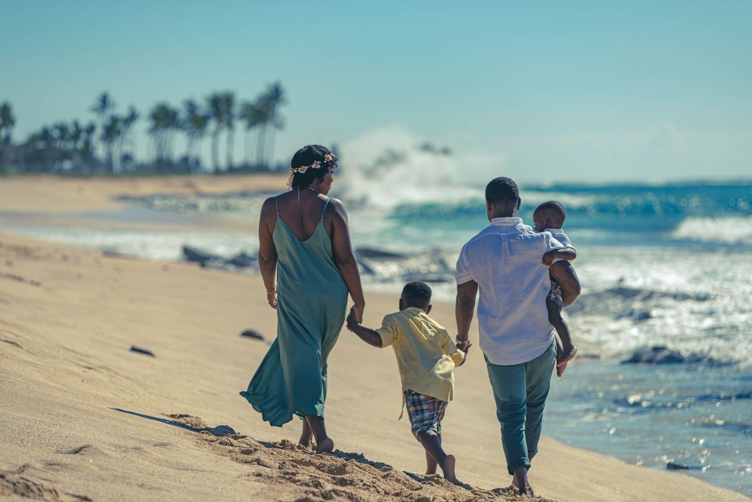 Family walking together along sandy beach with ocean waves in background.
