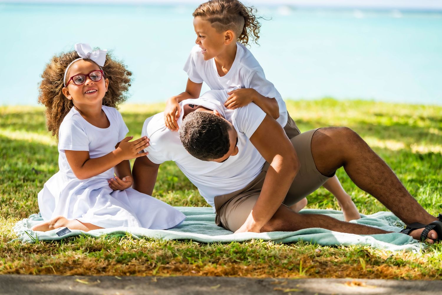 Family members lying on grass near beach sharing playful moments.