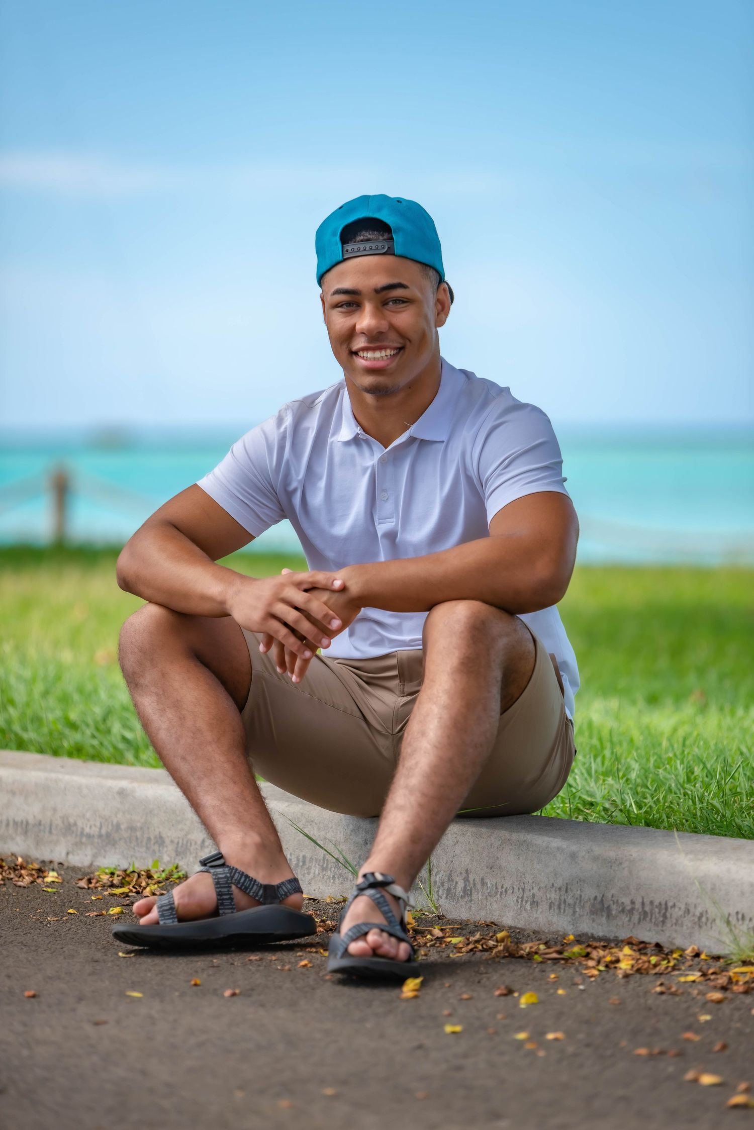 Casual outdoor photoshoot on grass with turquoise ocean in background.