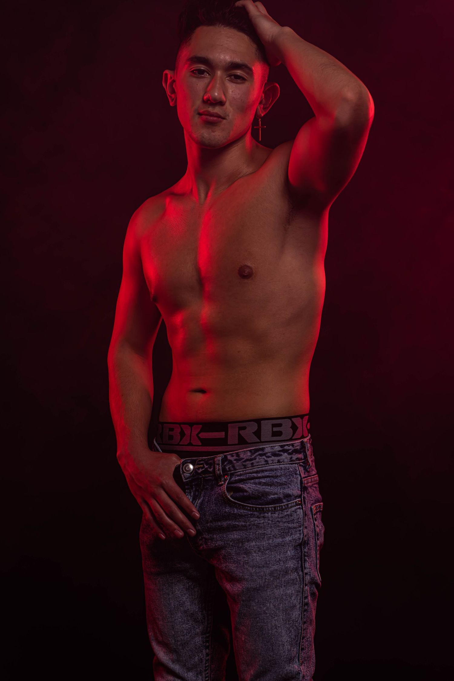 Moody portrait with red lighting showing torso in denim jeans.