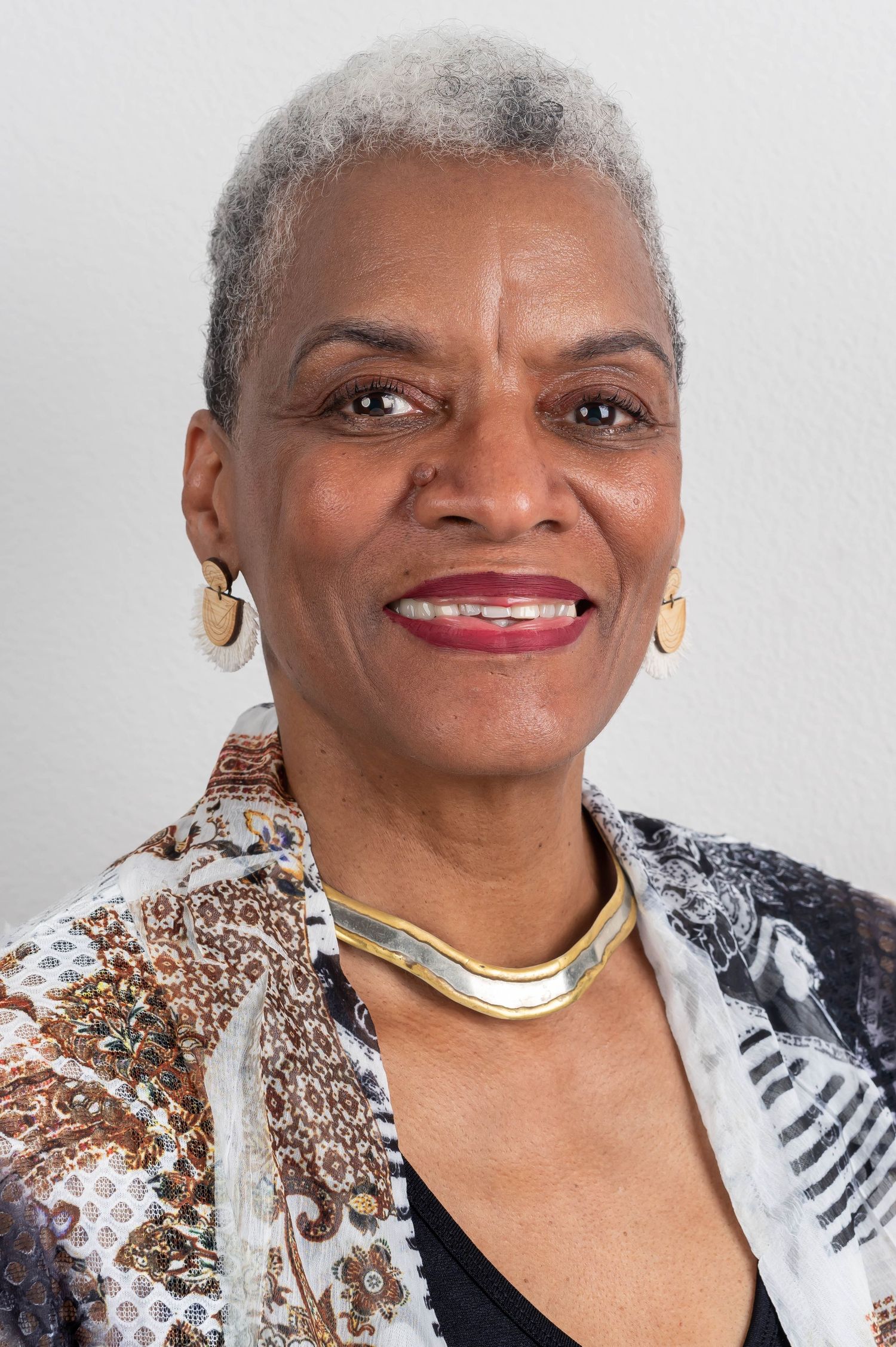 Portrait showing gold necklace and earrings with black and white patterned clothing.