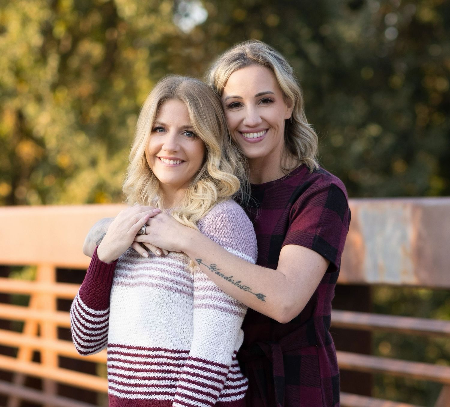 Two people in coordinating burgundy and striped outfits embrace outdoors during an autumn photoshoot.