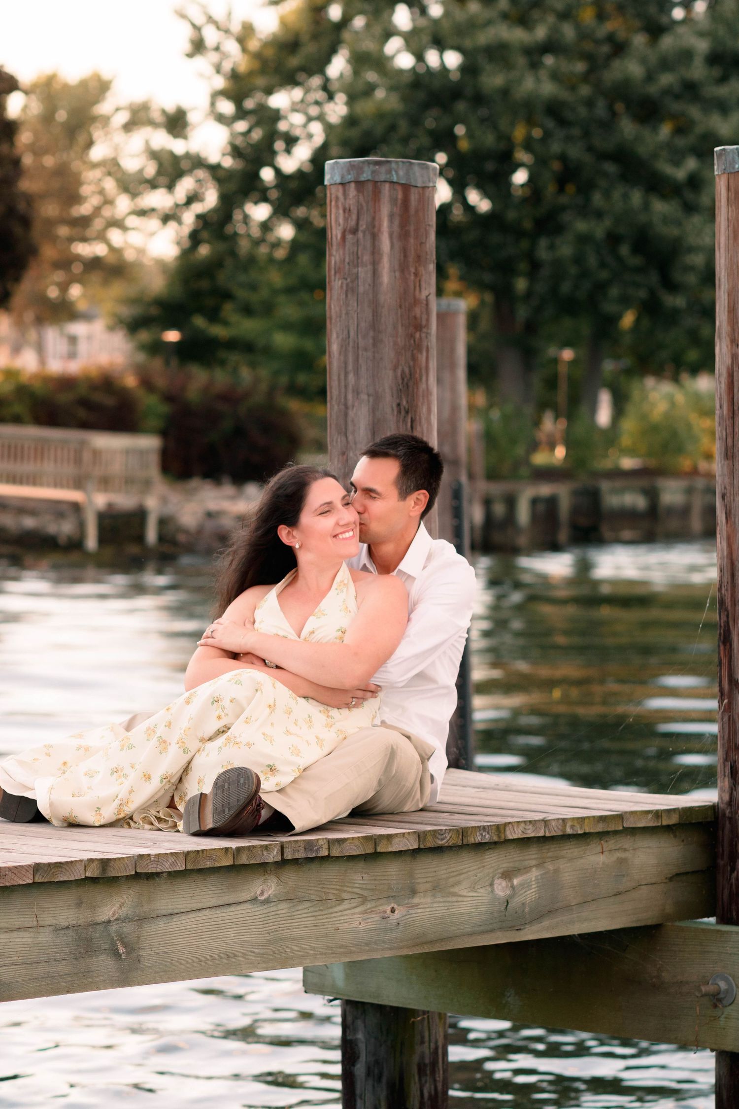 Couple lounging romantically on a wooden dock over water at sunset.