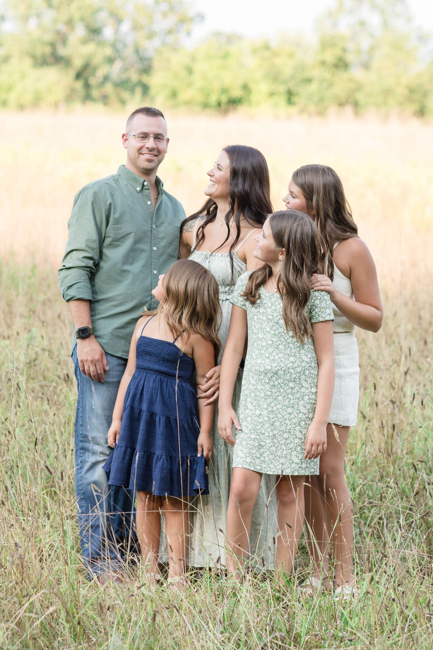 A group stands together in a sunlit meadow wearing coordinated outfits of green and navy blue.