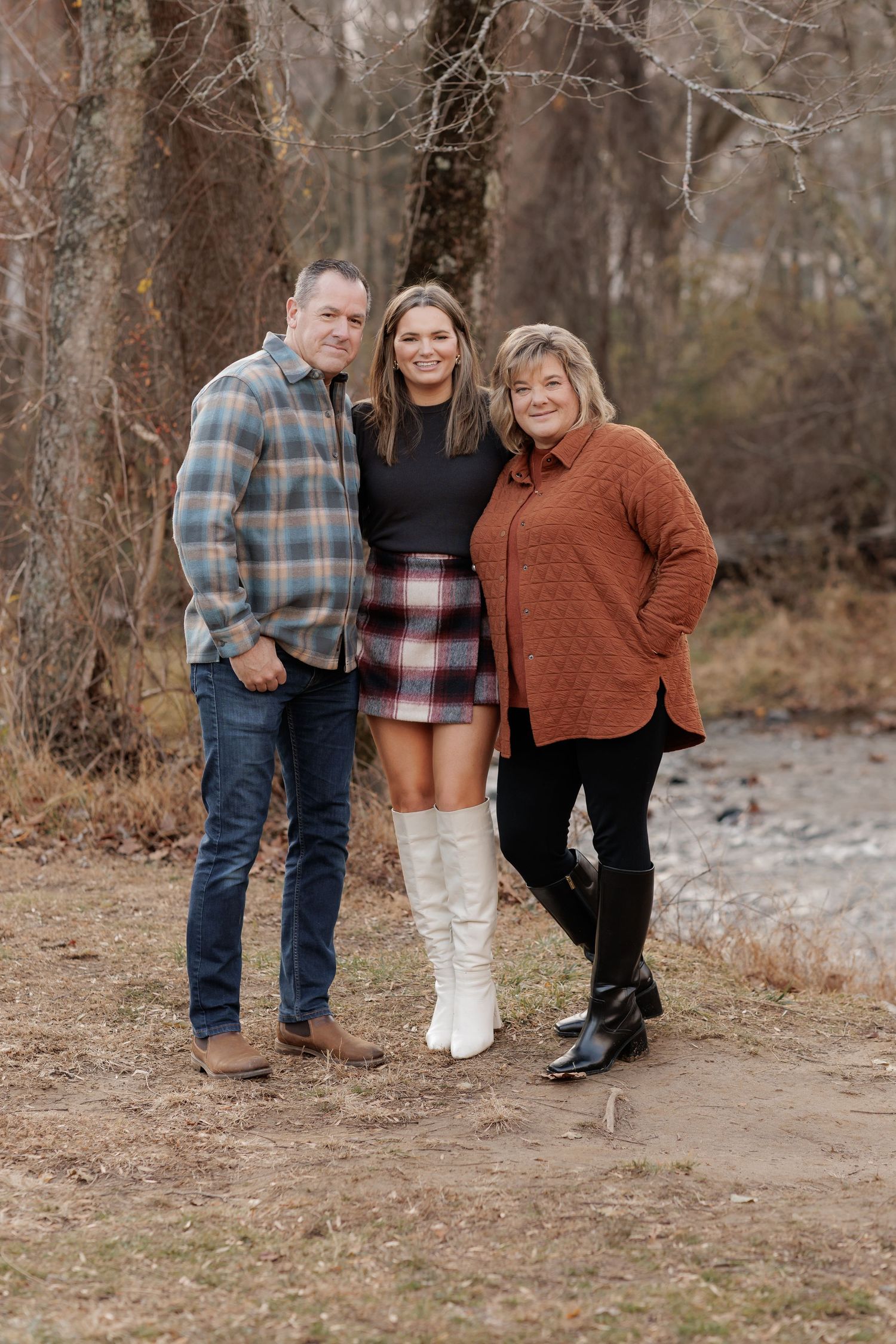 Group wearing cozy fall sweaters and plaid poses together in a wooded setting.