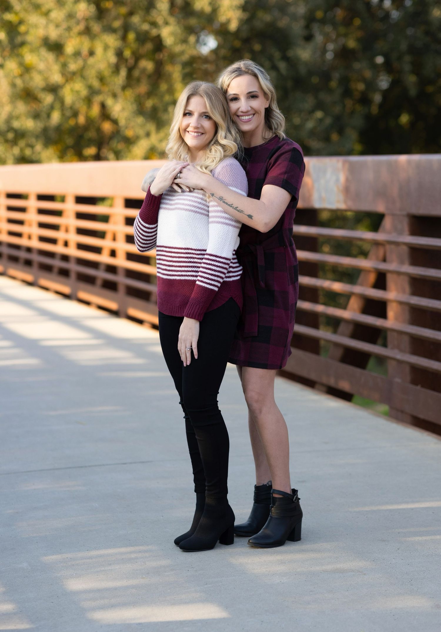 Two friends embrace on a wooden bridge during an outdoor photoshoot.