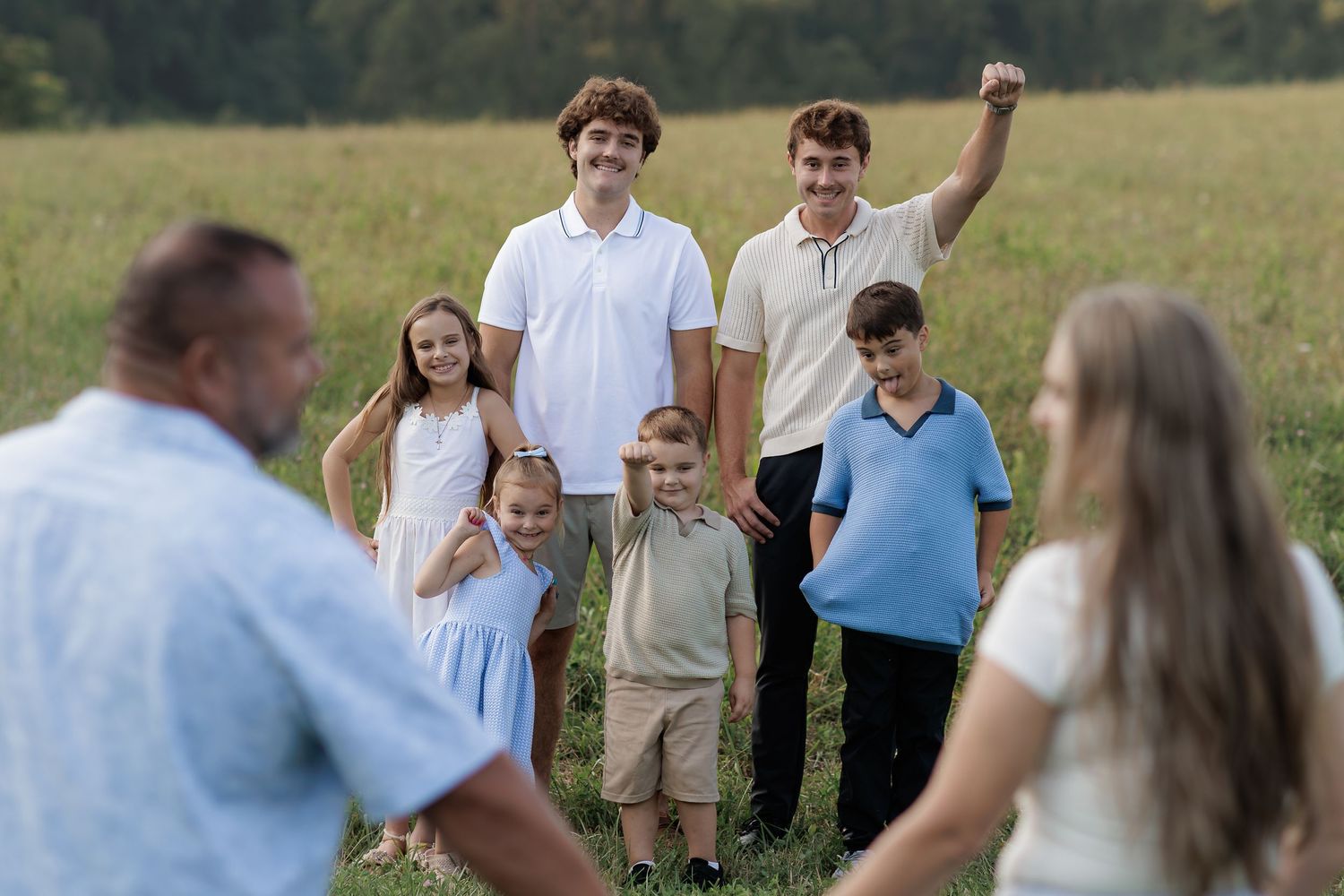 Family group photo with children and adults smiling in a green field during a sunny outdoor gathering.