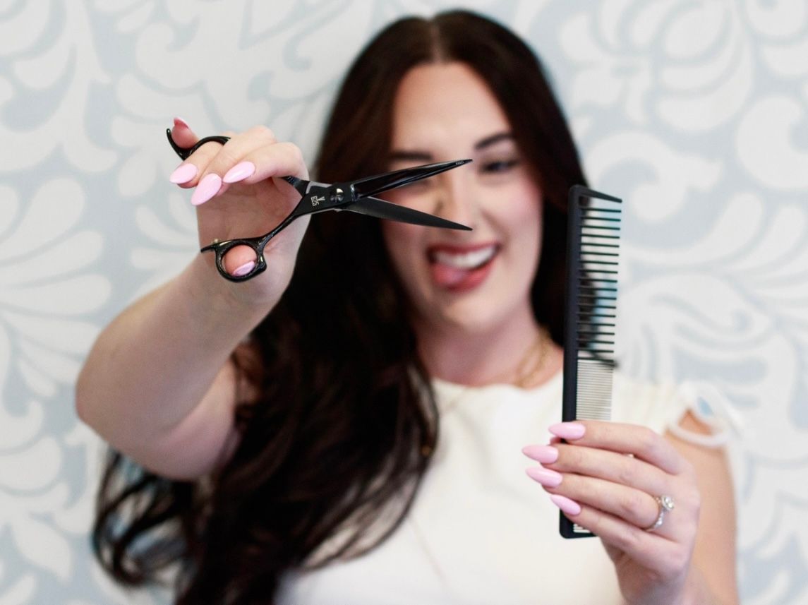 Close-up of hands holding hair styling tools against light background.