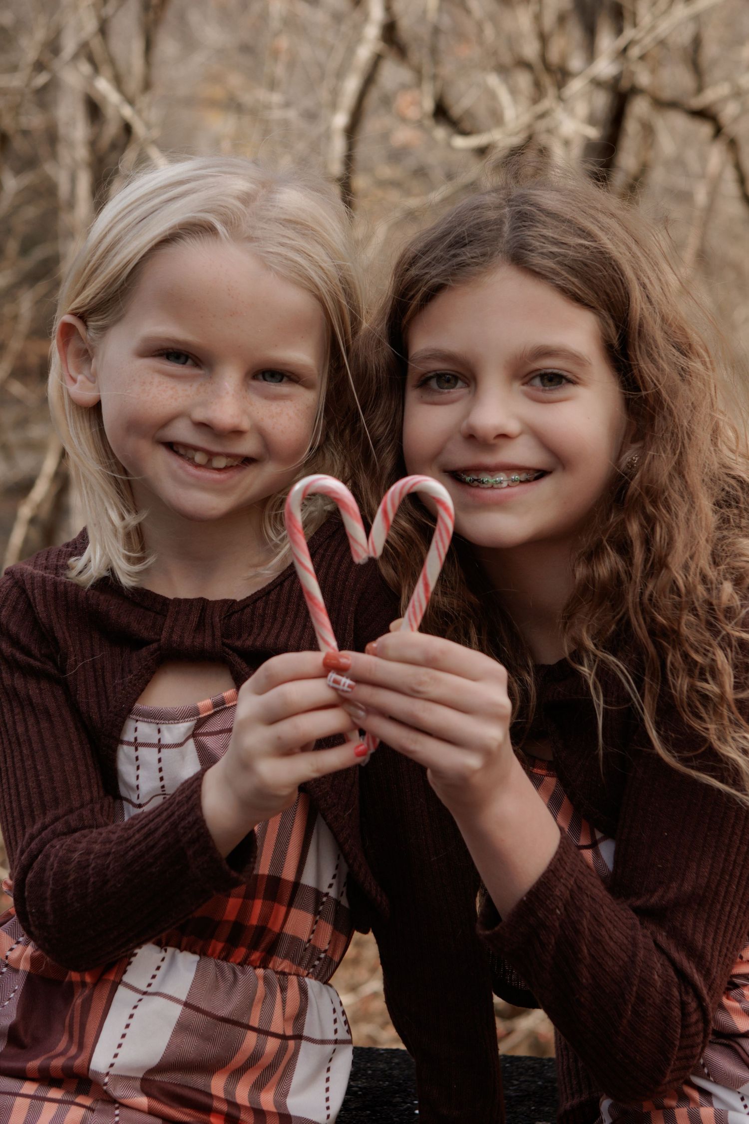 Two children holding candy canes to form a heart shape against a natural background.