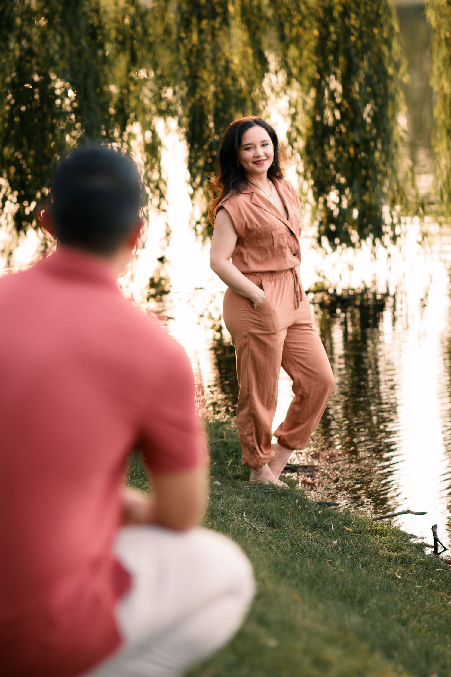Maternity photoshoot by a peaceful pond with willow trees at sunset.