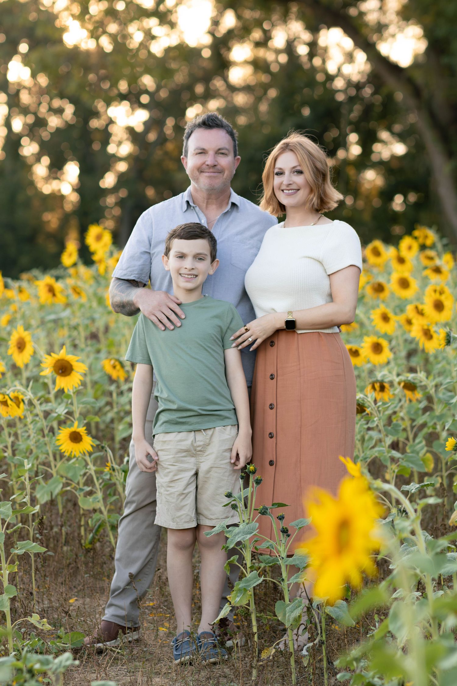 A family poses together in a vibrant sunflower field during golden hour sunset.
