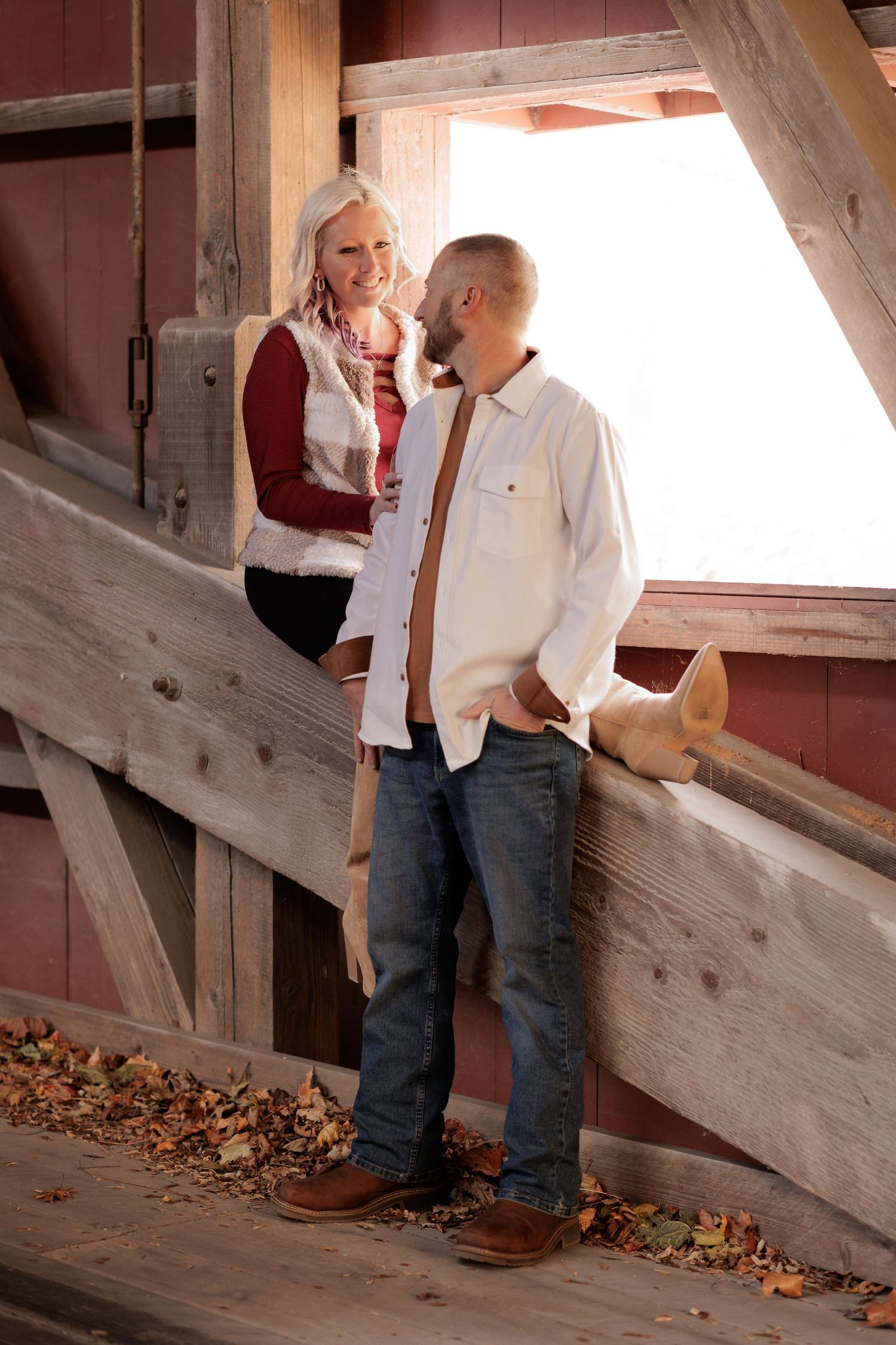 A couple shares playful moments inside a rustic wooden barn structure.