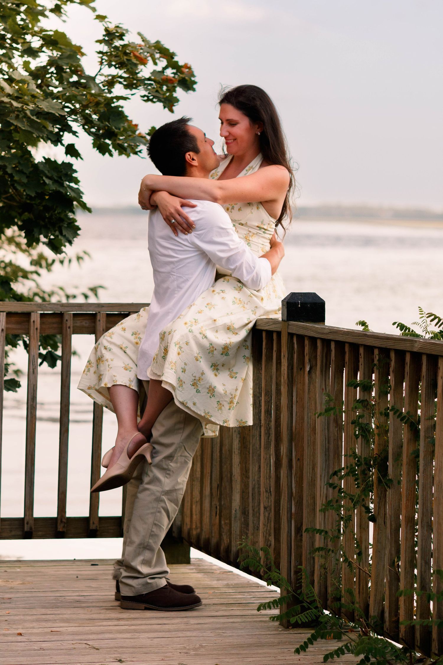 Playful couple dancing on a wooden deck overlooking the water.