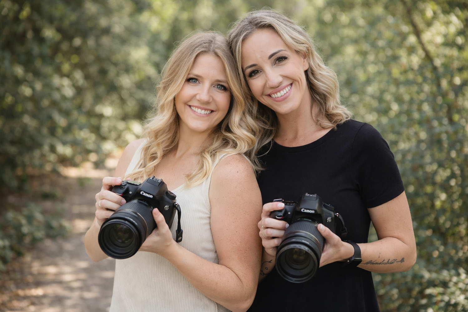 Two photographers with professional cameras pose together outdoors in a natural setting.
