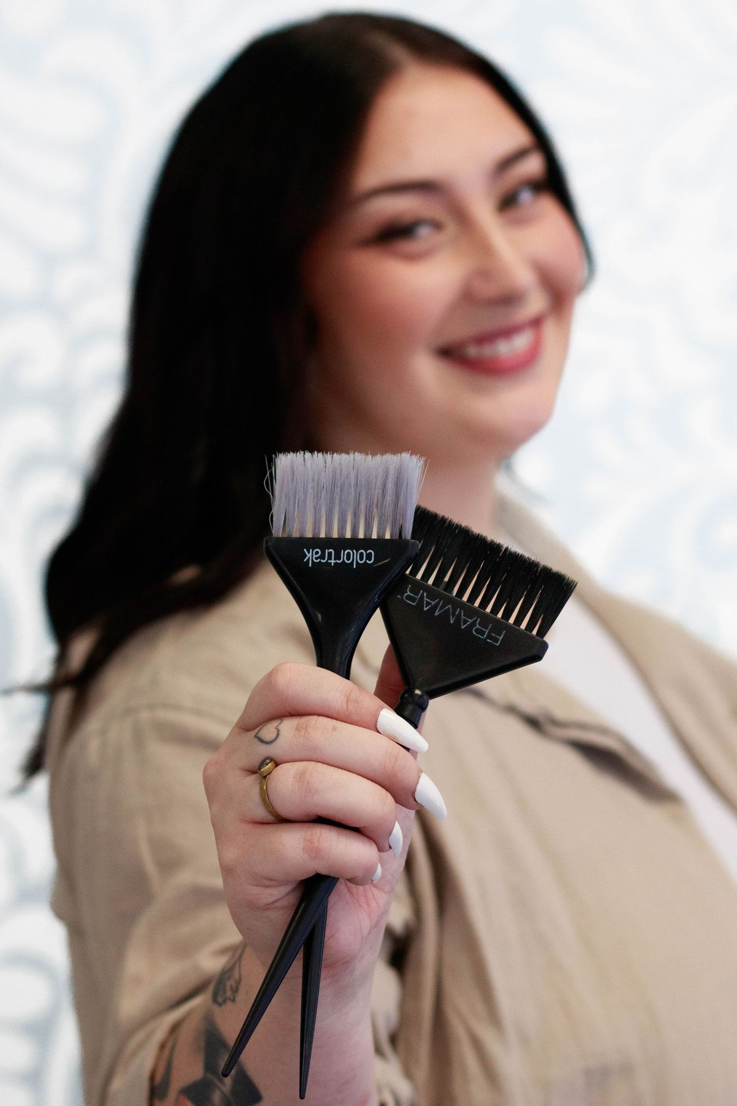 Professional holding multiple hair coloring brushes against white background.