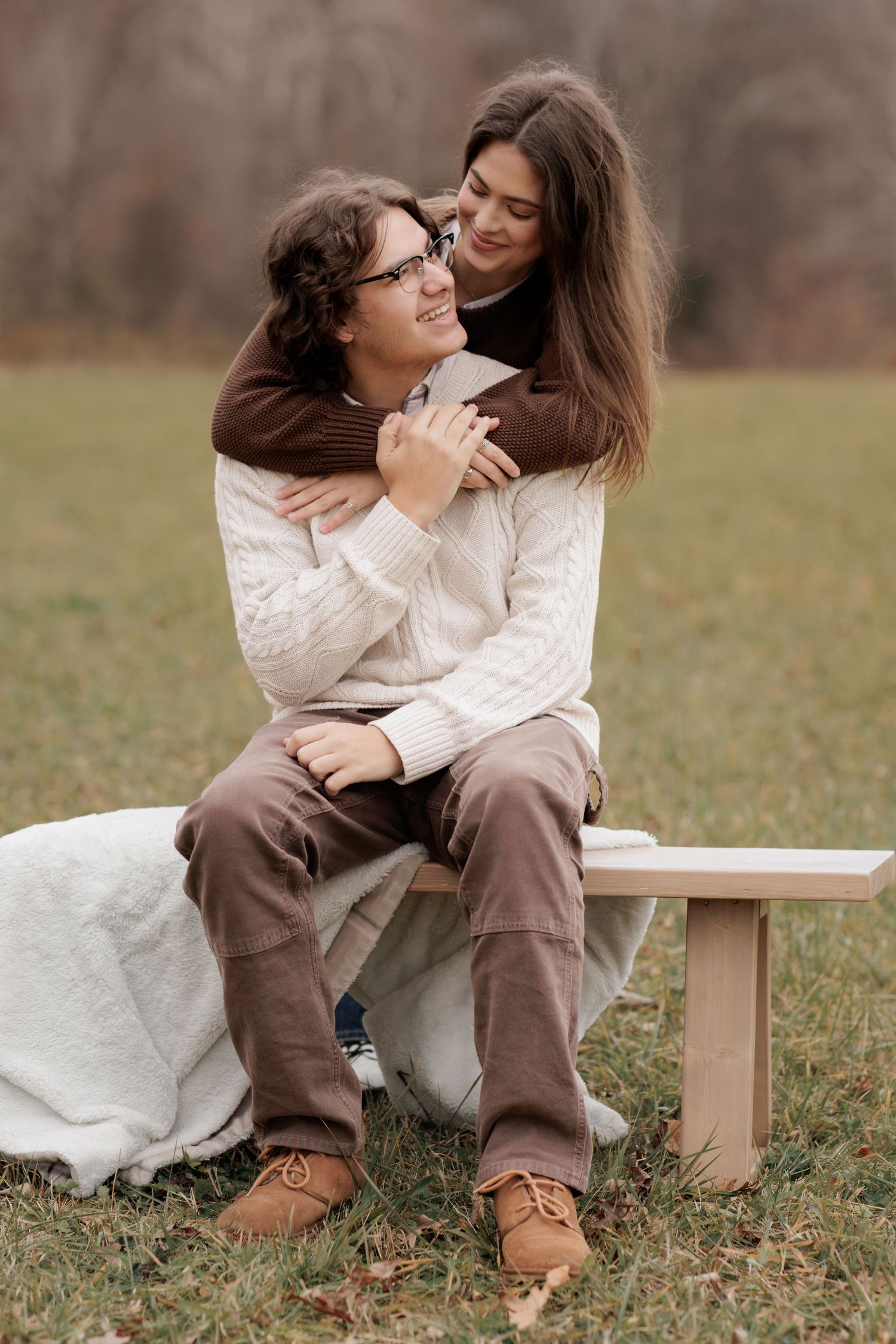 Tender embrace on wooden bench during outdoor autumn photoshoot.