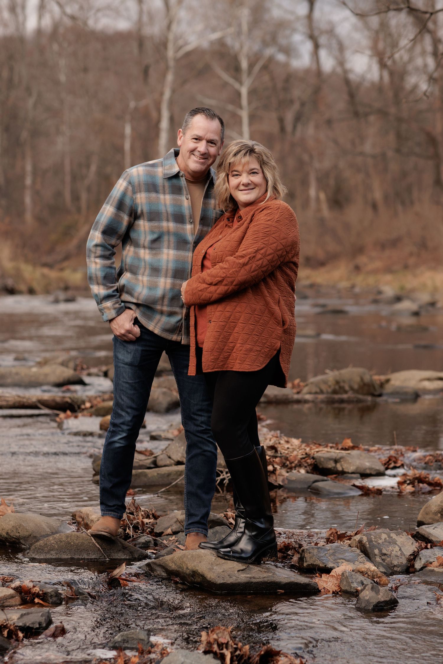 Couple stands together on rocky creek bed during autumn photo session.