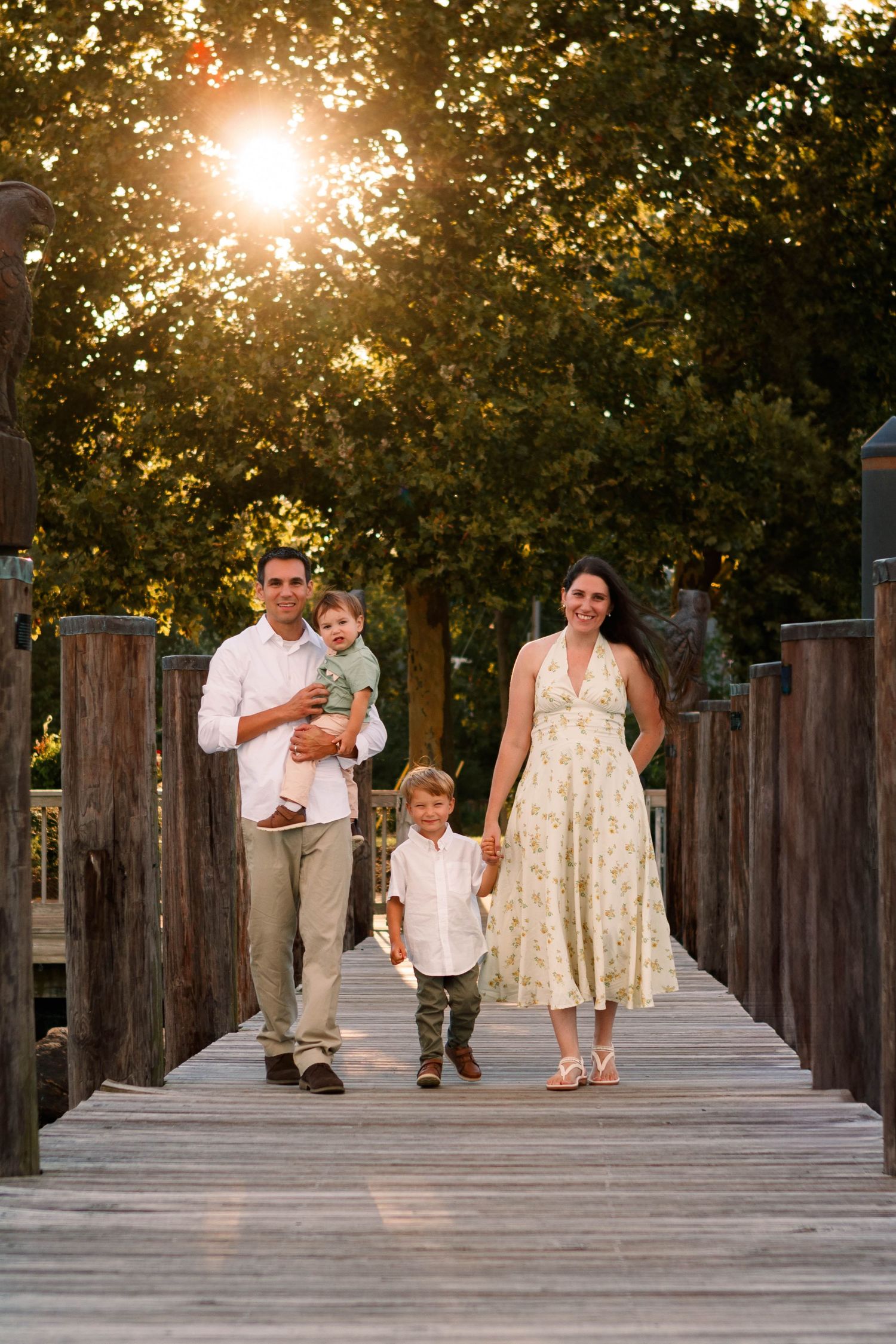 People strolling along a wooden boardwalk at golden hour with sunlight streaming through trees.