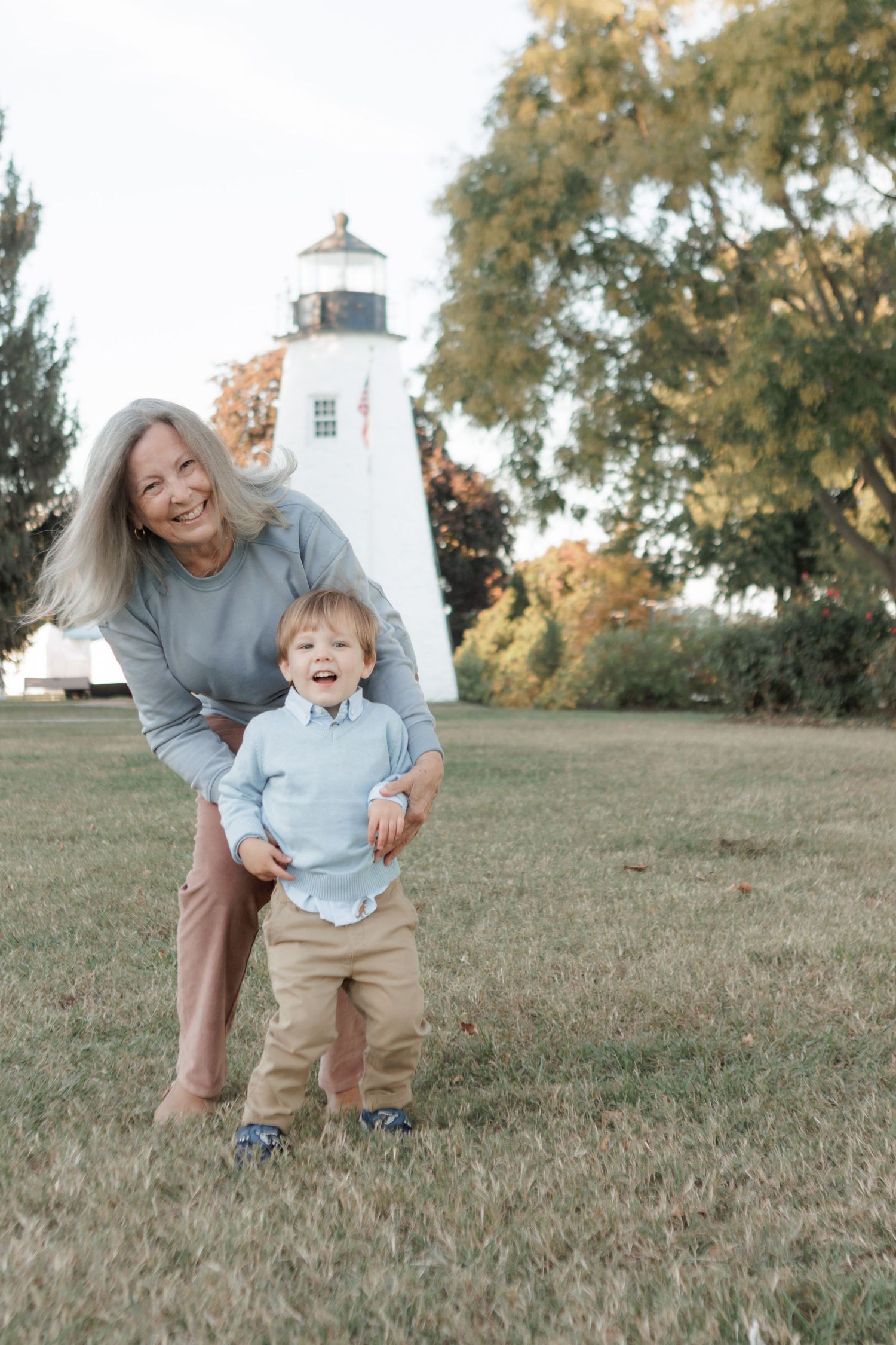 Playful moment captured near a white lighthouse on a grassy hill.