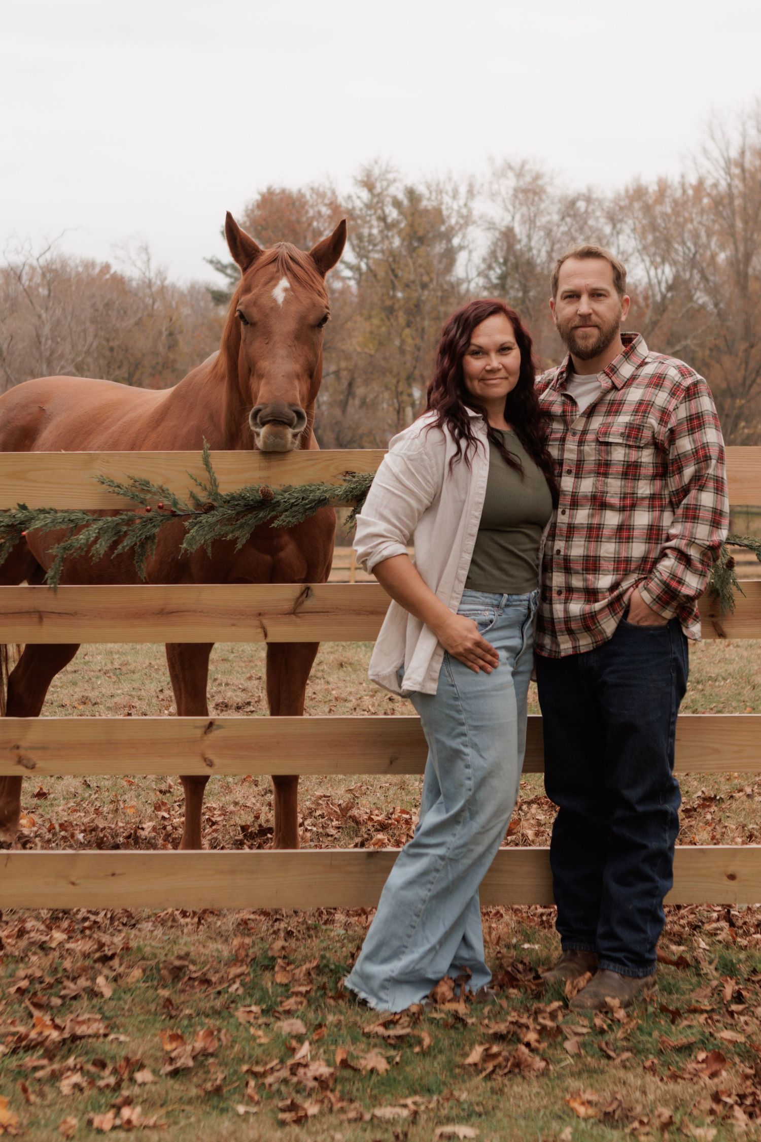 Romantic photoshoot by a wooden fence with horses in the background during autumn.