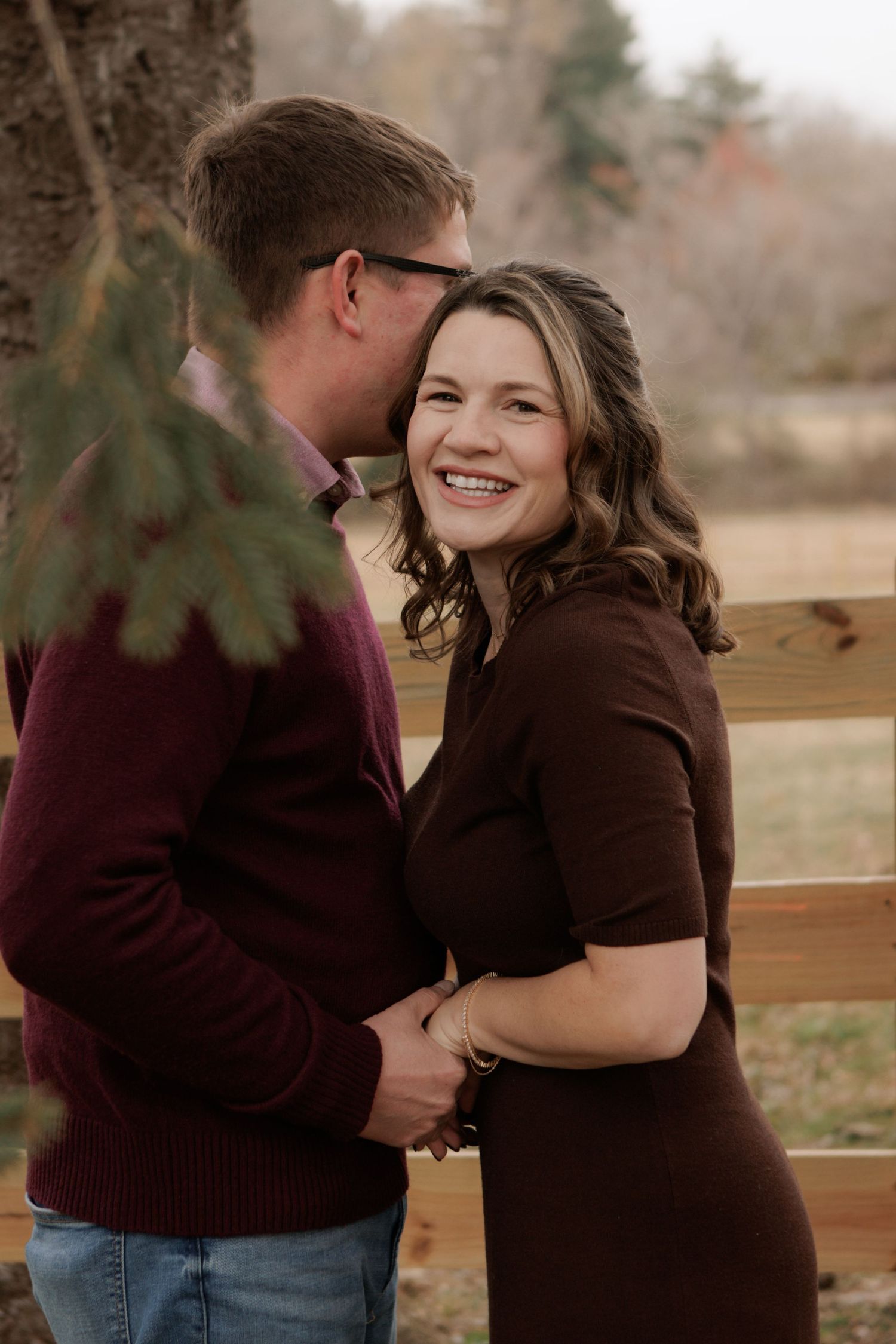 Couple sharing tender moments together on a wooden bench in casual fall attire.