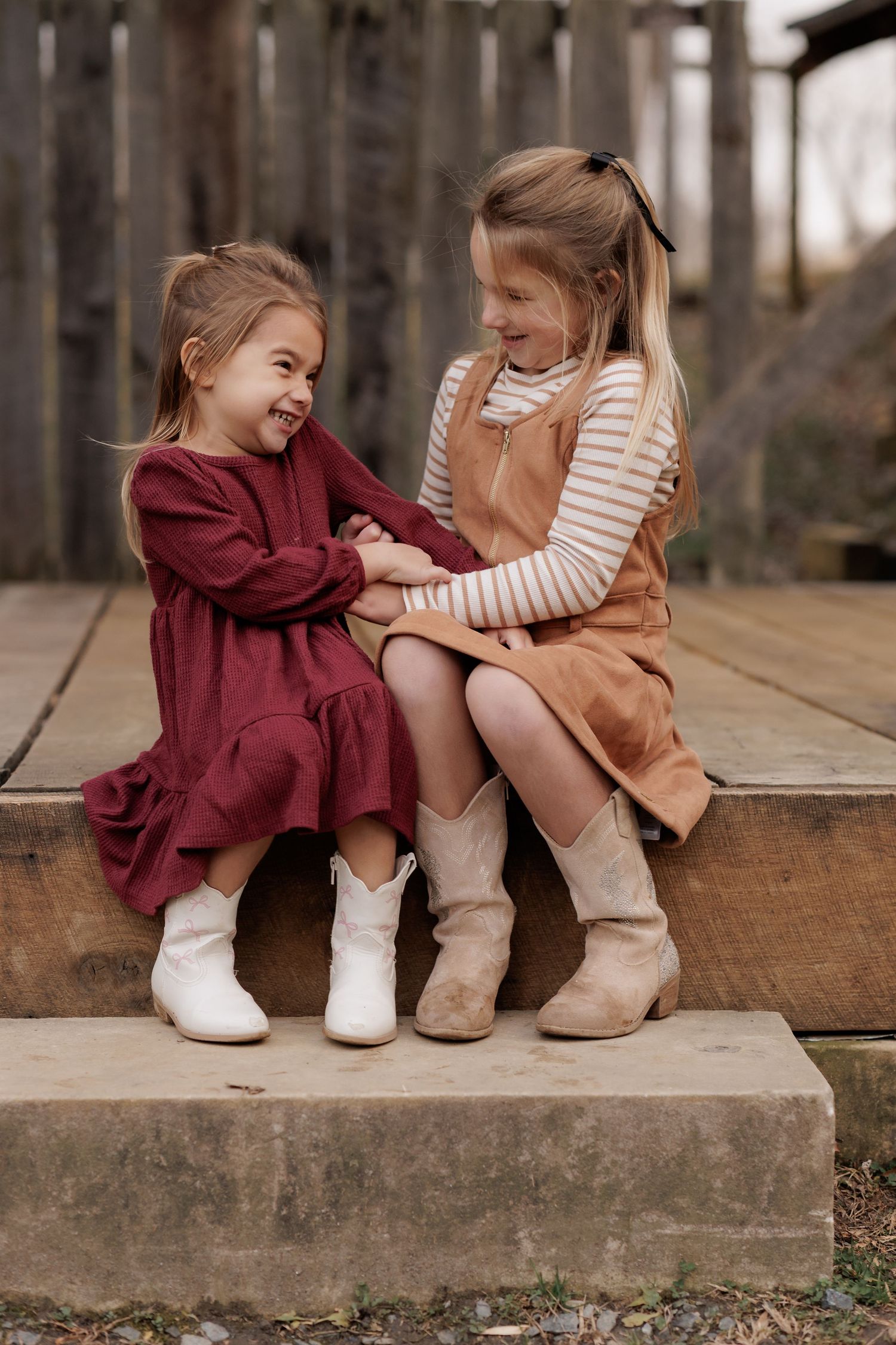Children in burgundy and tan outfits sitting together on wooden steps outdoors.