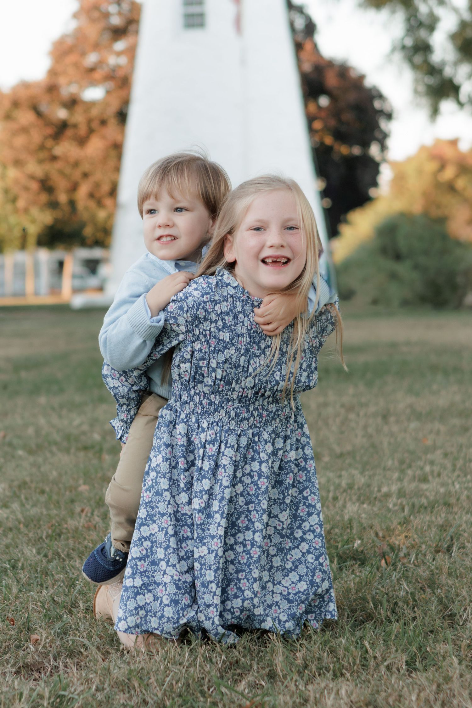 Two children play together and laugh while sitting on grass during a sunny autumn day.