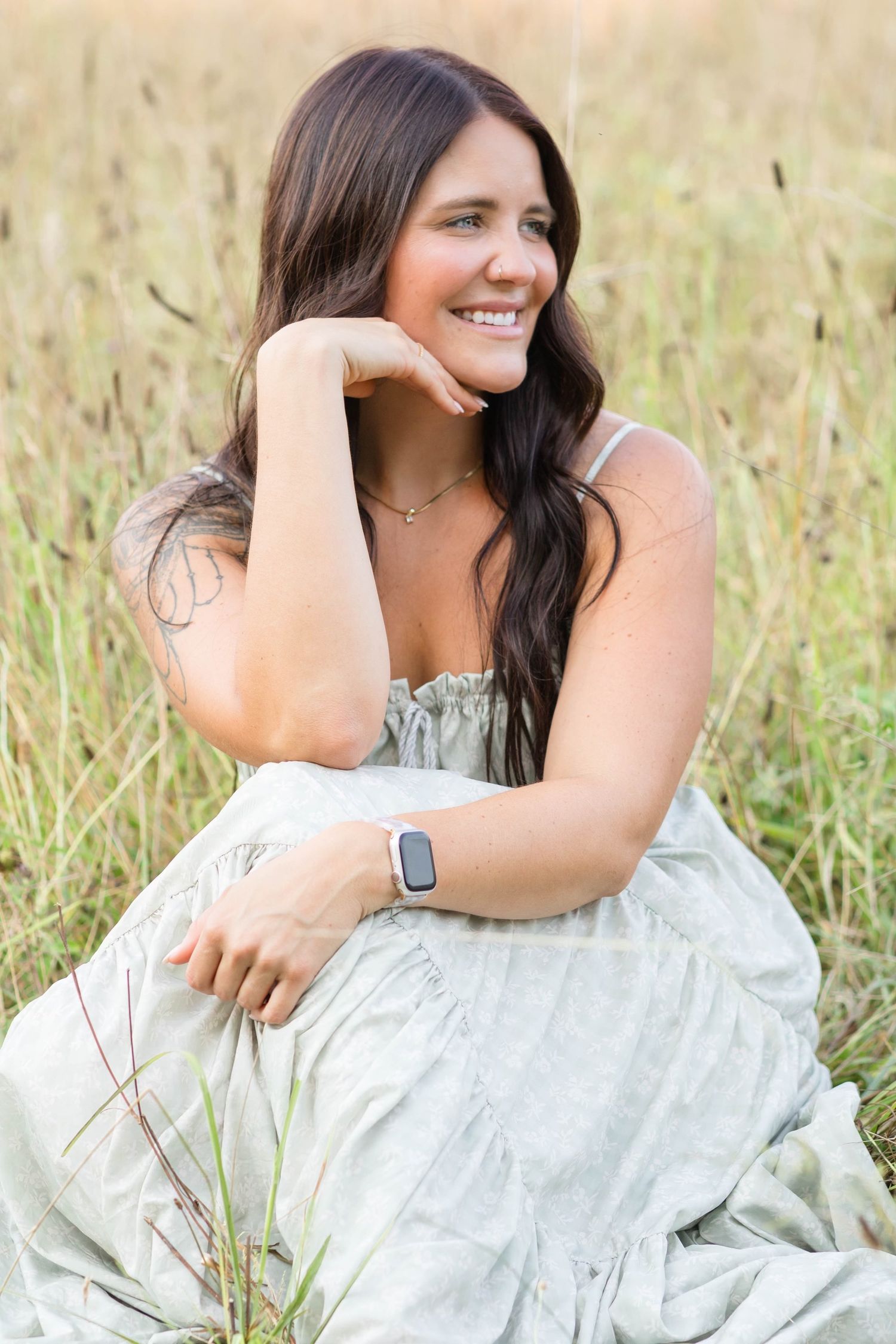 A person in a white dress sits in a grassy field while posing for outdoor portrait photographs.