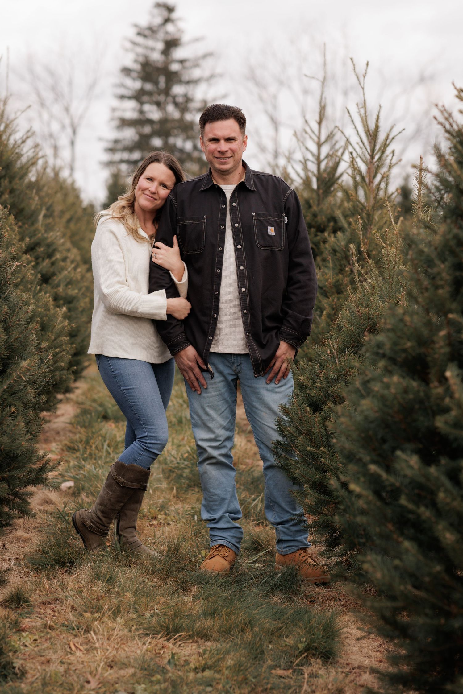 Casual couple posing together at a Christmas tree farm.