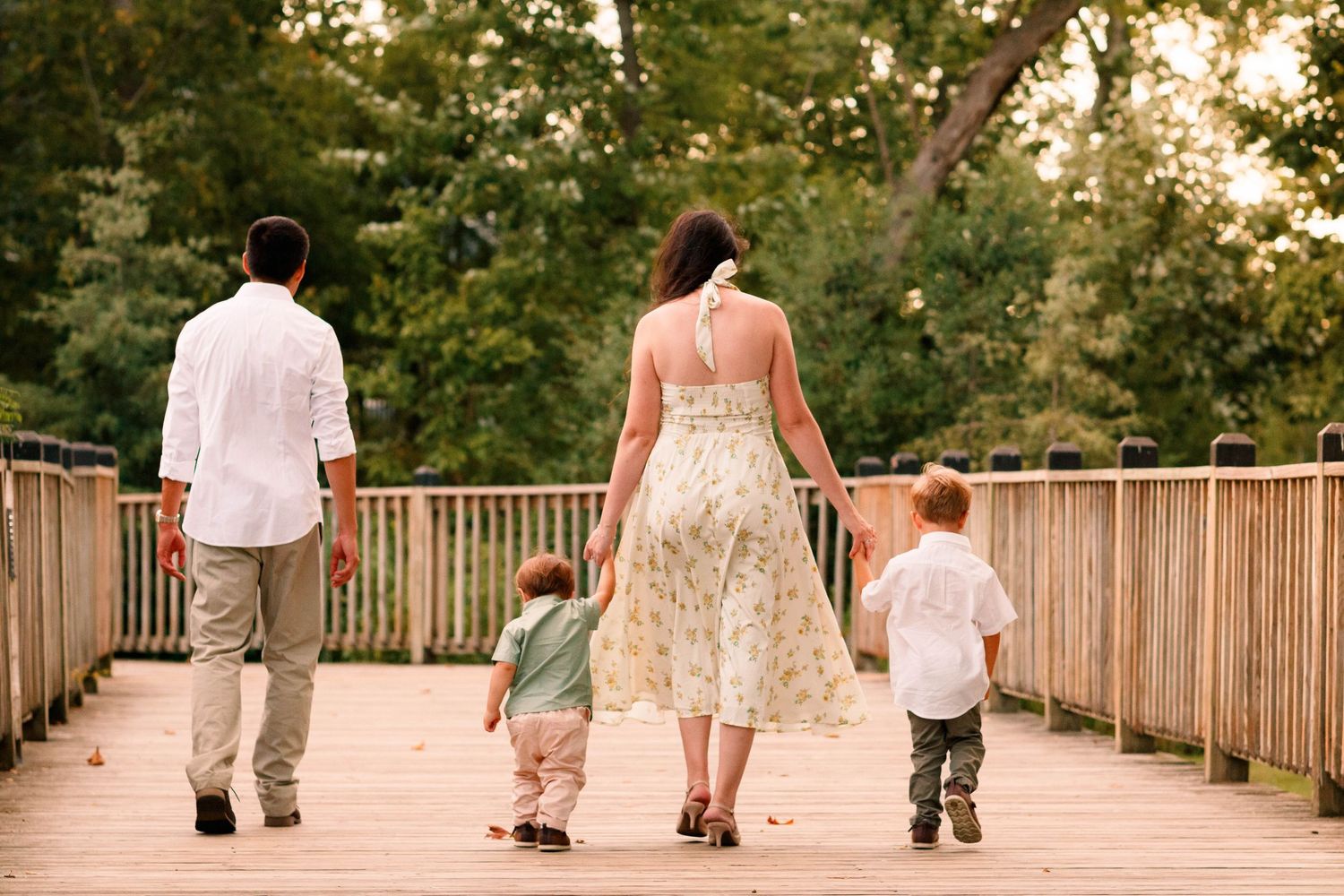 Family walking together on a wooden boardwalk at sunset through a park.
